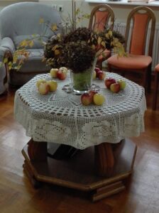 Jesienny biukiet i jabłka na stole przykrytym białą serwetą; w tle krzesła i fotel 