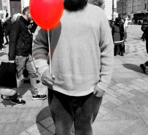 Człowiek trzymający czerwony balon zamocowany na białej rurce