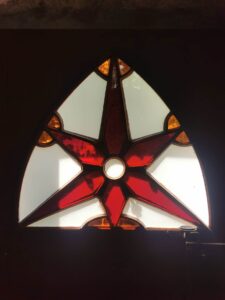Czerwono-biały witraż w formie gwiazdy umieszczony w drzwiach do kaplicy nagrobnej w Piotrawinie nad Wisłą