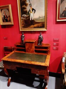 Ozdobne drewniane biurko z dwoma metalowymi statuetkami stojące na tle czerwonej ściany