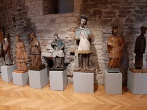 Siedem drewnianych figur Świętych eksponowanych na drewnianych kubikach