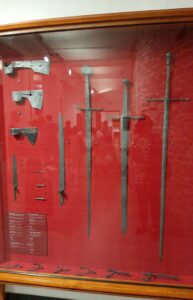 Stalowe miecze, ostrogi, topory i strzały eksponowane na czerwonej tkaninie