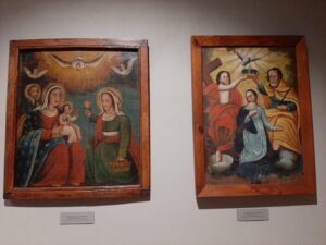 Wiszące na ścianie dwa obrazy z nurtu malarstwa ludowego przedstawiające Świętą Rodzinę i Koronację Maryi
