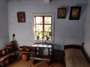 Izba w drewnianej chałupie w skansenie z widocznymi glinianymi naczyniami i wiszącymi obrazami