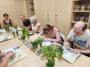 Pięć osób siedzących przy stole i ugniatających zioła w ceramicznych pojemnikach