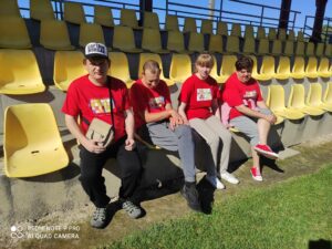 Cztery osoby w czerwonych koszulkach siedzące na stadionowej trybunie