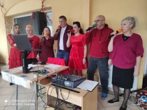 Siedem dorosłych osób w czerwonych ubraniach i trzymających mikrofony w dłoni