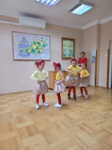Czworo dzieci w pomieszczeniu ubranych w żółte t-shirty czerwone rajstopy i czerwone chustki na głowach