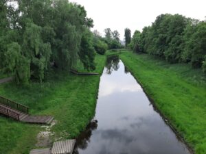 Fragment uregulowanej rzeki otoczony zielenią i widocznymi dwoma drewnianymi zejściami do nadbrzeża