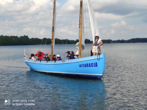 Duża łódź z niebieskim kadłubem wypełniona ludźmi i płynąca po jeziorze