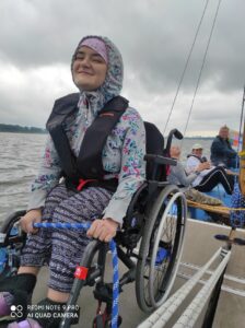 Uśmiechnięta kobieta siedząca na wózku inwalidzkim umieszczonym na pokładzie płynącej łodzi