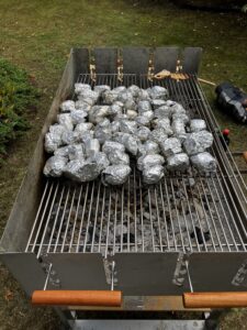 Duża ilość ziemniaków pozawijanych w srebrną folię i ułożonych na prostokątnym grillowym ruszcie