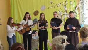 Pięcioosobowa grupa we wnętrzu trzymająca instrumenty i teksty w dłoniach