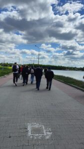 Grupa dorosłych osób widziana z tyłu i spacerująca nadbrzeżem wyłożonym szarą kostką