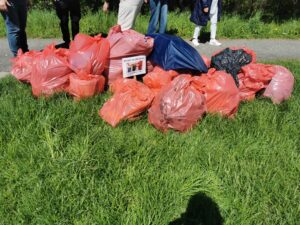 Leżące na zielonej trawie kilkanaście czerwonych worków wypełnionych śmieciami