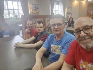 Czterech mężczyzn siedzących przy stole we wnętrzu i patrzących w stronę osoby fotografującej