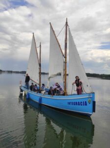 Dwumasztowa łódź z niebieskim kadłubem i grupą dorosłych osób na pokładzie