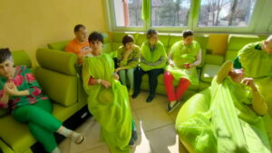 Grupa dorosłych osób przebranych w zielone powłóczyste szaty i siedząca na zielonych kanapkach