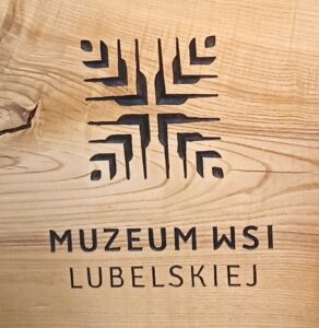 Geometryczne logo Muzeum Wsi Lubelskiej wypalone na jasnym drewnie