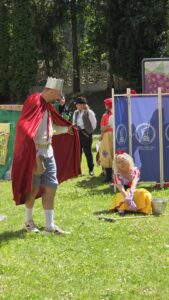 Mężczyzna przebrany za króla i kobieta przebrana za królewnę na tle kolorowych parawanów ustawionych na trawie