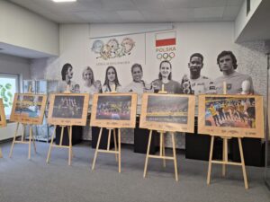 Pięć dużych fotografii z zawodnikami siatkarskimi ustawionych na drewnianych sztalugach a w tle czarno-białe sylwetki sportowców związanych z Lubelszczyzną naklejone na białej ścianie