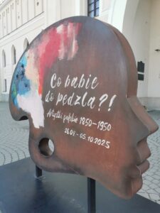 Duża forma przestrzenna w kształcie głowy i jednocześnie palety pokrytej farbami oraz napisem informacyjnym o wystawie