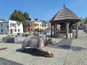 Duży wybrukowany plac otoczony piętrowymi domami ze znajdującą się na nim drewanianą studnią i rzeźbą niedźwiedzia naturalnych rozmiarów