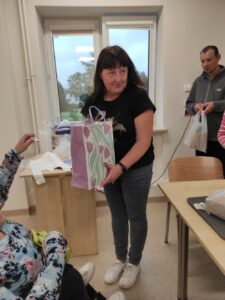 Kobieta z ciemnymi włosami trzymająca w dłoniach dużą papierową fioletowo-zieloną torbę