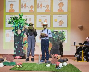 Dwóch mężczyzn w kapeluszach stojących w leśnej scenografii a w tle wyświetlone liczne kwadraty z piktogramami