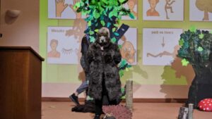 Osoba przebrana za zwierzę i stojąca w leśnej scenografii a w tle wyświetlone liczne kwadraty z piktogramami