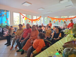 Dorośli i dzieci w ubraniach o pomarańczowym kolorze siedzący na krzesłach w jasnej sali