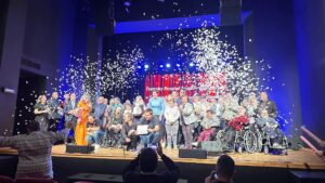 Duża ilość osób stojących na drewnianej scenie i spadające białe konfetti