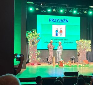 Na scenie z leśną scenografią stojących dwoje dorosłych w kapeluszach