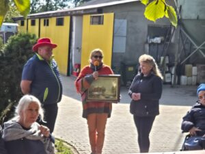 Trzy dorosłe osoby stojące na tle budynków stajni z żółtymi drzwiami