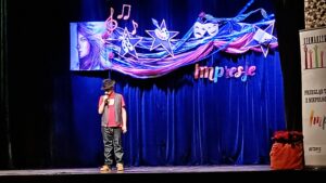 Mężczyzna w kapeluszu trzymający mikrofon i stojący na scenie z niebieską kotarą