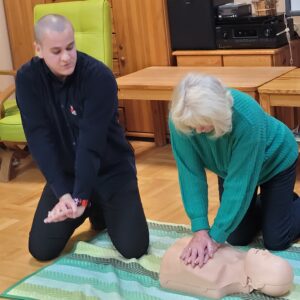 Starsza kobieta instruowana przez mężczyznę wykonuje uciski okolicy międzymostkowej na fantomie