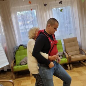 Starsza kobieta obejmuje od tyłu mężczyznę w treningowej kamizelce do robienia uścisków