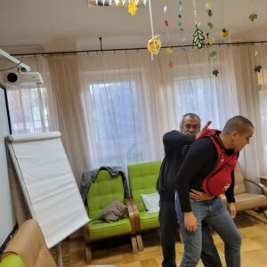 Starszy mężczyzna wykonuje od tyłu uderzenie odkrztuszeniowe na mężczyźnie w treningowej kamizelce