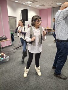 Trzy dorosłe osoby stojące na szarej wykładzinie na tle białych i różowych ścian