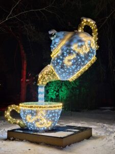 Plenerowa i kolorowa iluminacja świetlna z wielu lampek w formie przechylonego czajnika nad filiżnaką