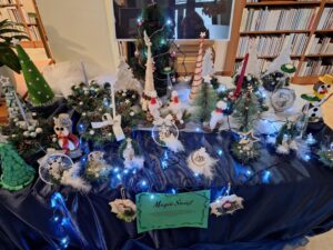 Rękodzielnicze ozdoby związane ze świętami Bożego Narodzenia ustawione wśród choinkowych lampek na stole nakrytym granatowym materiałem