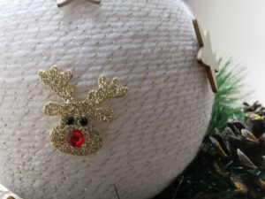 Zbliżenie bombki wykonanej z białej wełny z naklejonymi na niej elementami w kształcie gwiazd i reniferów