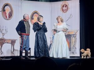 Scena rodzajowa z przedstawienia teatralnego z dwoma kobietami w balowych sukniach mężczyzną w mundurze huzara i psem