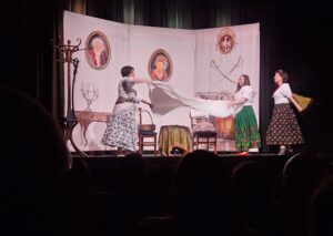 Scena rodzajowa z przedstawienia teatralnego z trzema kobietami w kolorowych spódnicach składającymi prześcieradło