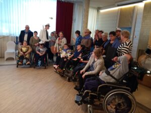 We wnętrzu grupa osób na wózkach inwalidzkich a za nim druga grupa stojąca