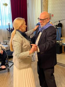 We wnętrzu tańcząca para - kobieta w białej plisowanej sukience i żakiecie w paski oraz mężczyzna w garniturze