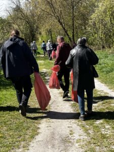 Grupa dorosłych osób z czerwonymi workami idąca po szerokiej ścieżce wśród zieleni