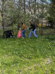 Trzy dorosłe osoby z czerwonym workiem idące po terenie zielonym
