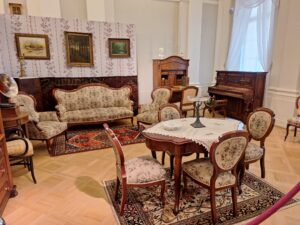 Zabytkowy komplet mebli salonowych z pianinem eksponowany w pałacowym wnętrzu