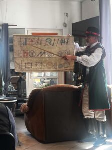 Mężczyzna w tradycyjnym kaszubskim stroju trzymający tablicę z kolorowymi symbolami graficznymi